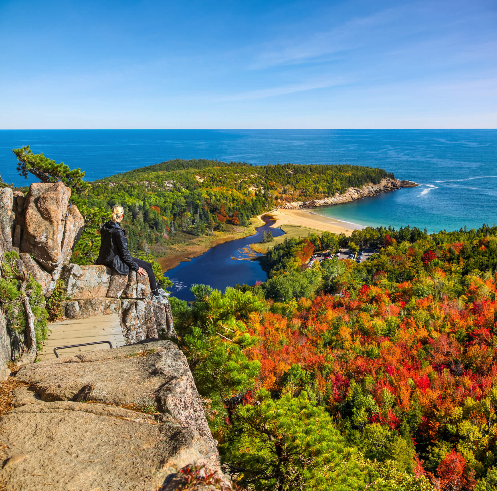Woman sitting on rock outcrop above beautiful fall trees and water Woman sitting on rock outcrop above beautiful fall trees and water