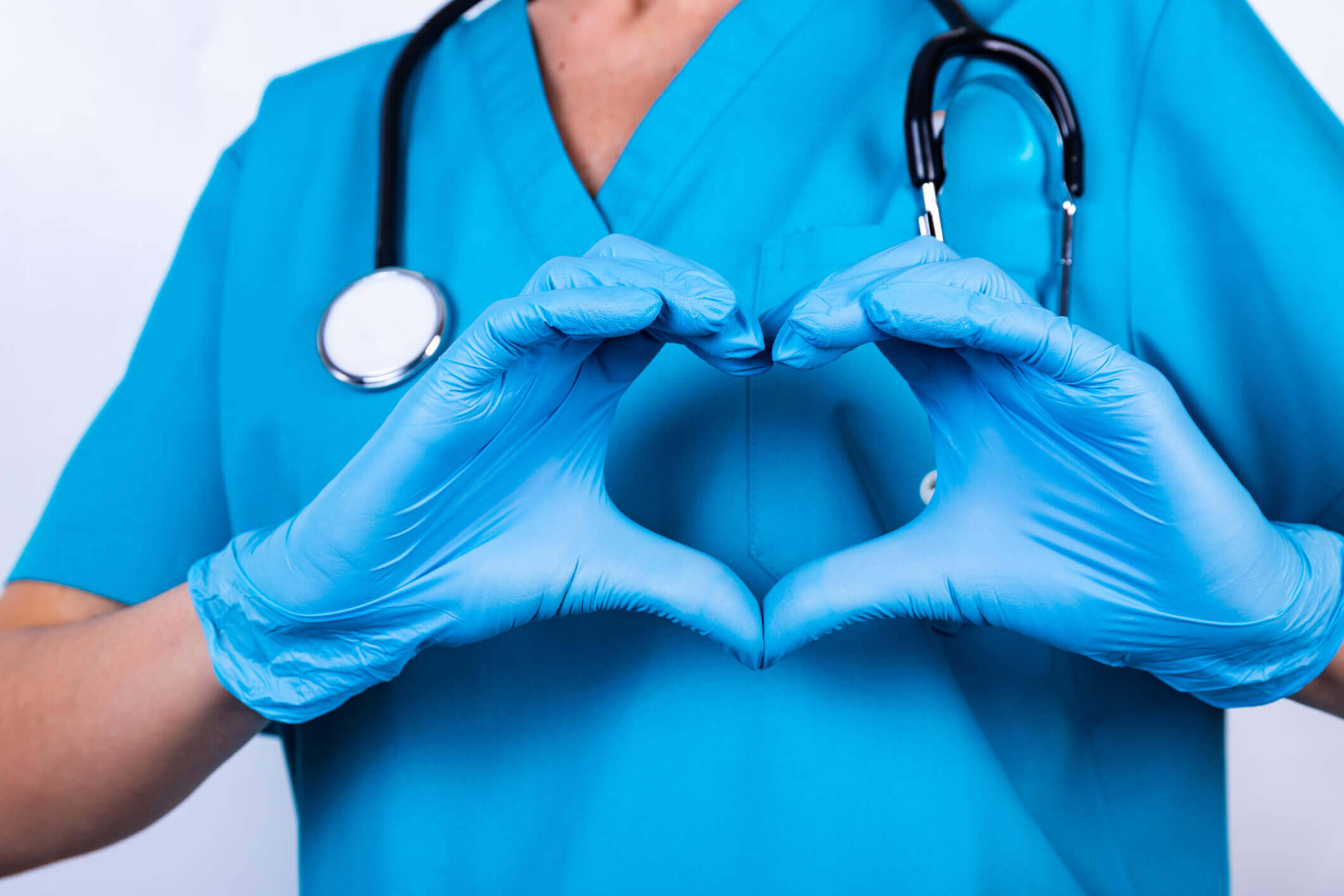 close up of woman in blue scrubs and gloves making a heart with hands over chest close up of woman in blue scrubs and gloves making a heart with hands over chest