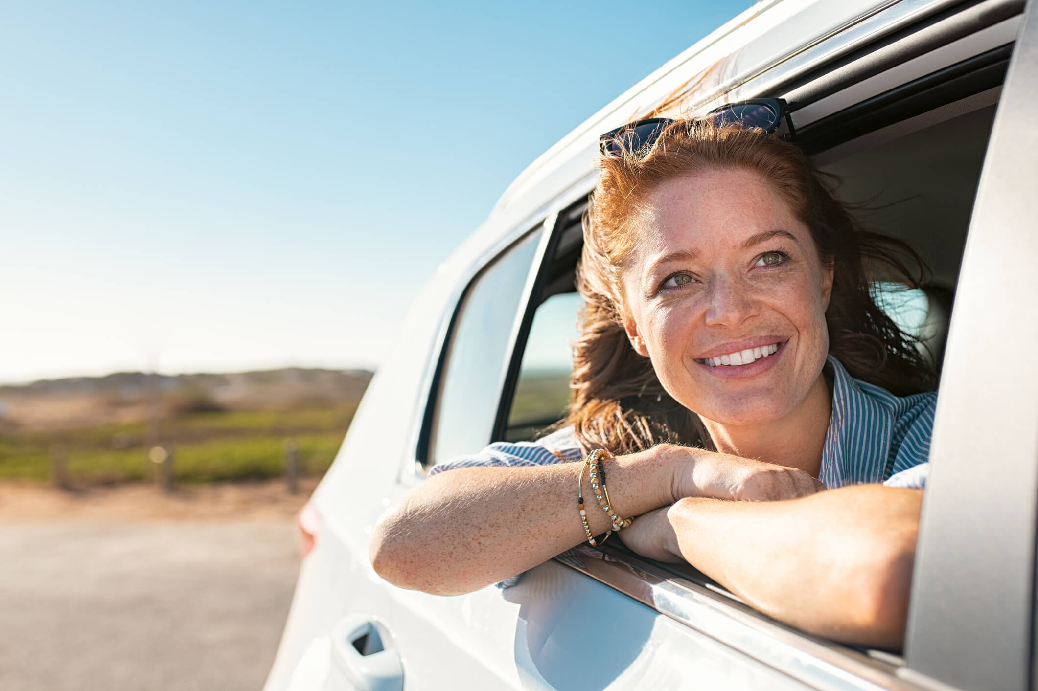 woman looking out car window, smiling, with arms crossed on sill woman looking out car window, smiling, with arms crossed on sill