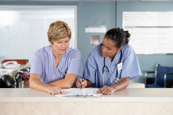 Two nurses reviewing paperwork together at nurses station Two nurses reviewing paperwork together at nurses station