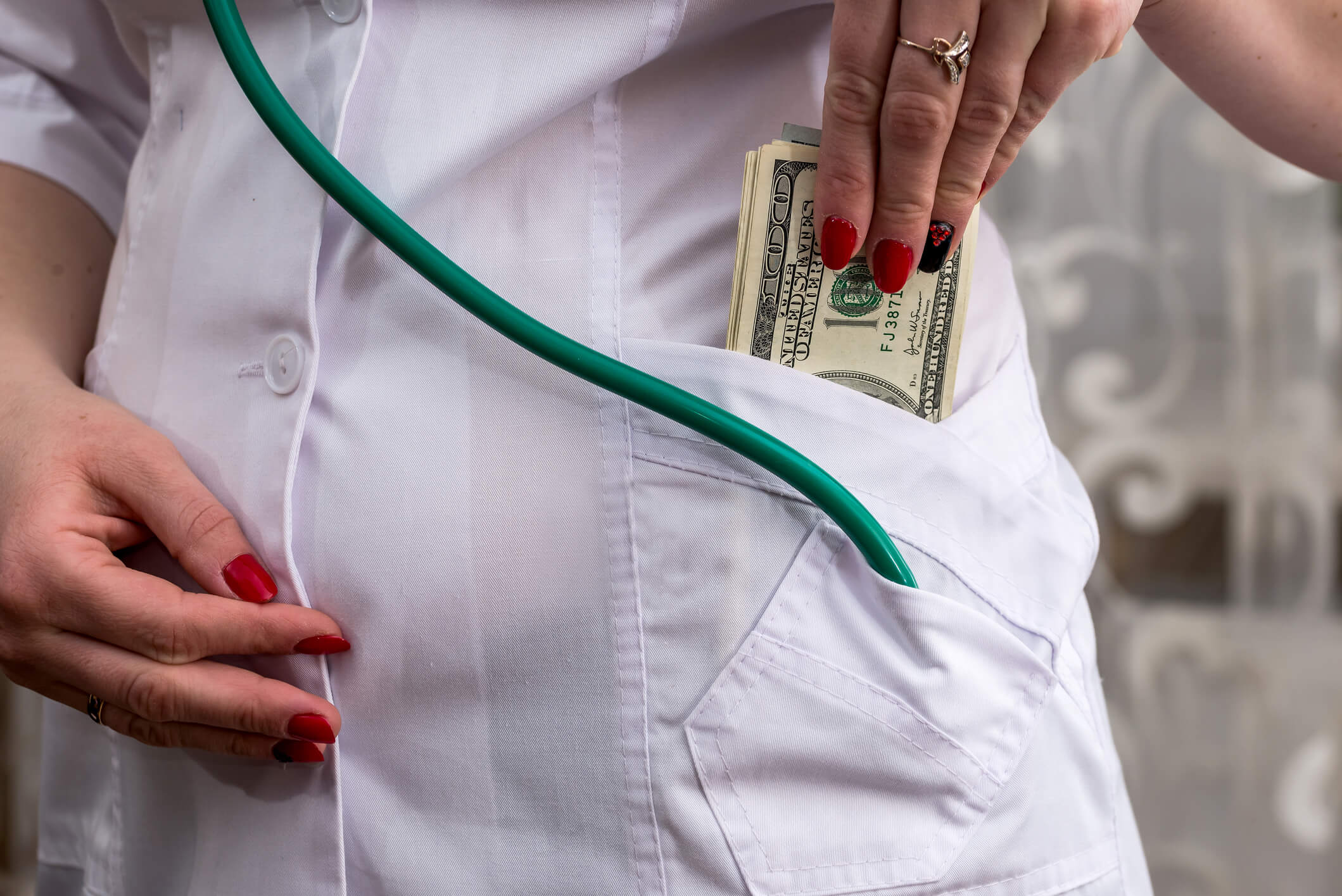 Professional in lab coat with stethoscope putting cash in pocket Professional in lab coat with stethoscope putting cash in pocket