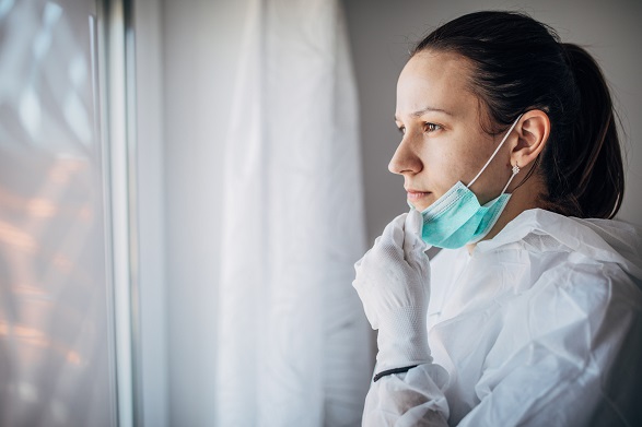 Healthcare worker looks out window with mask pulled down below mouth Healthcare worker looks out window with mask pulled down below mouth