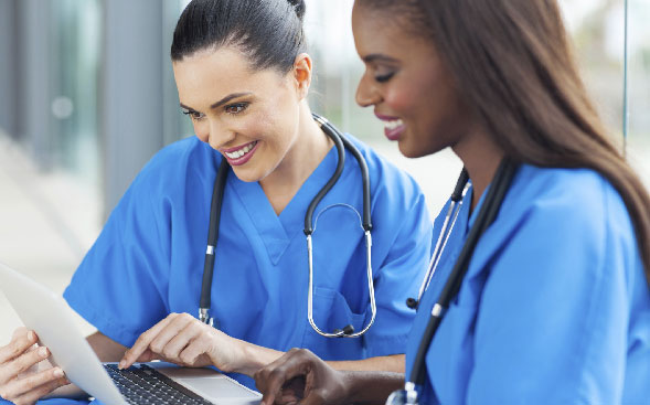 close up of two nurses smiling at something on laptop screen close up of two nurses smiling at something on laptop screen