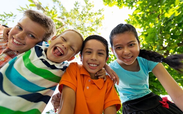 4 smiling kids, heads together, looking down at camera 4 smiling kids, heads together, looking down at camera