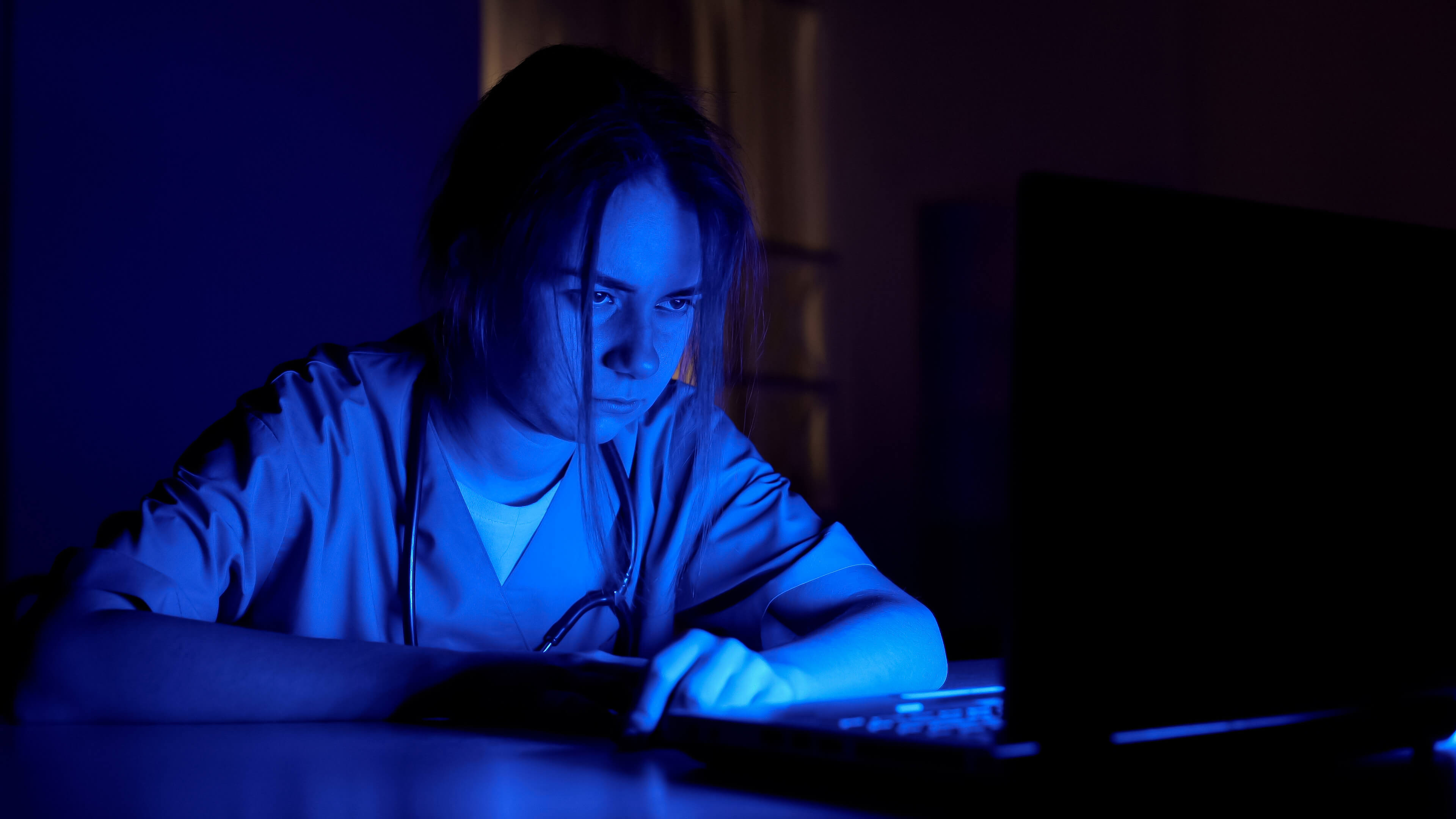 tired healthcare professional in dark room lit by computer screen tired healthcare professional in dark room lit by computer screen