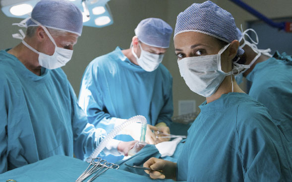 Masked OR nurse looking at camera while other colleagues work on patient Masked OR nurse looking at camera while other colleagues work on patient