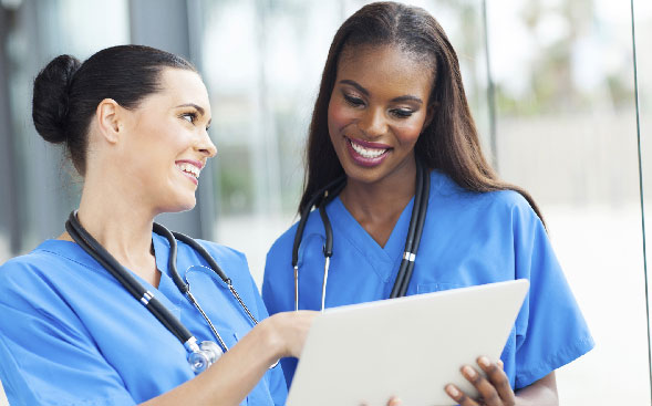 one smiling nurse showing laptop screen to another one smiling nurse showing laptop screen to another