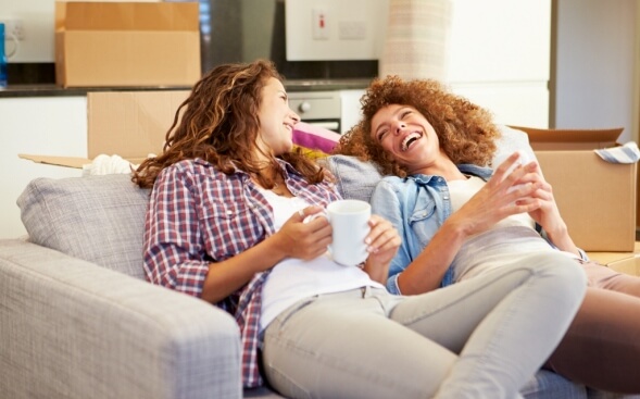 two woman relaxing with mugs on couch two woman relaxing with mugs on couch
