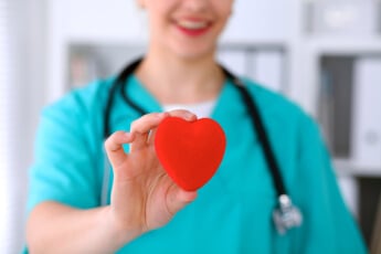 woman in scrubs holding a heart toward camera woman in scrubs holding a heart toward camera