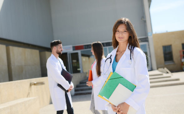 female graduate standing with cap in hand, other grads behind female graduate standing with cap in hand, other grads behind