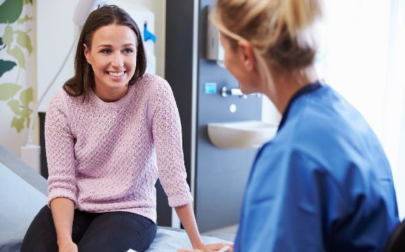 female patient sitting on bed talking to nurse female patient sitting on bed talking to nurse