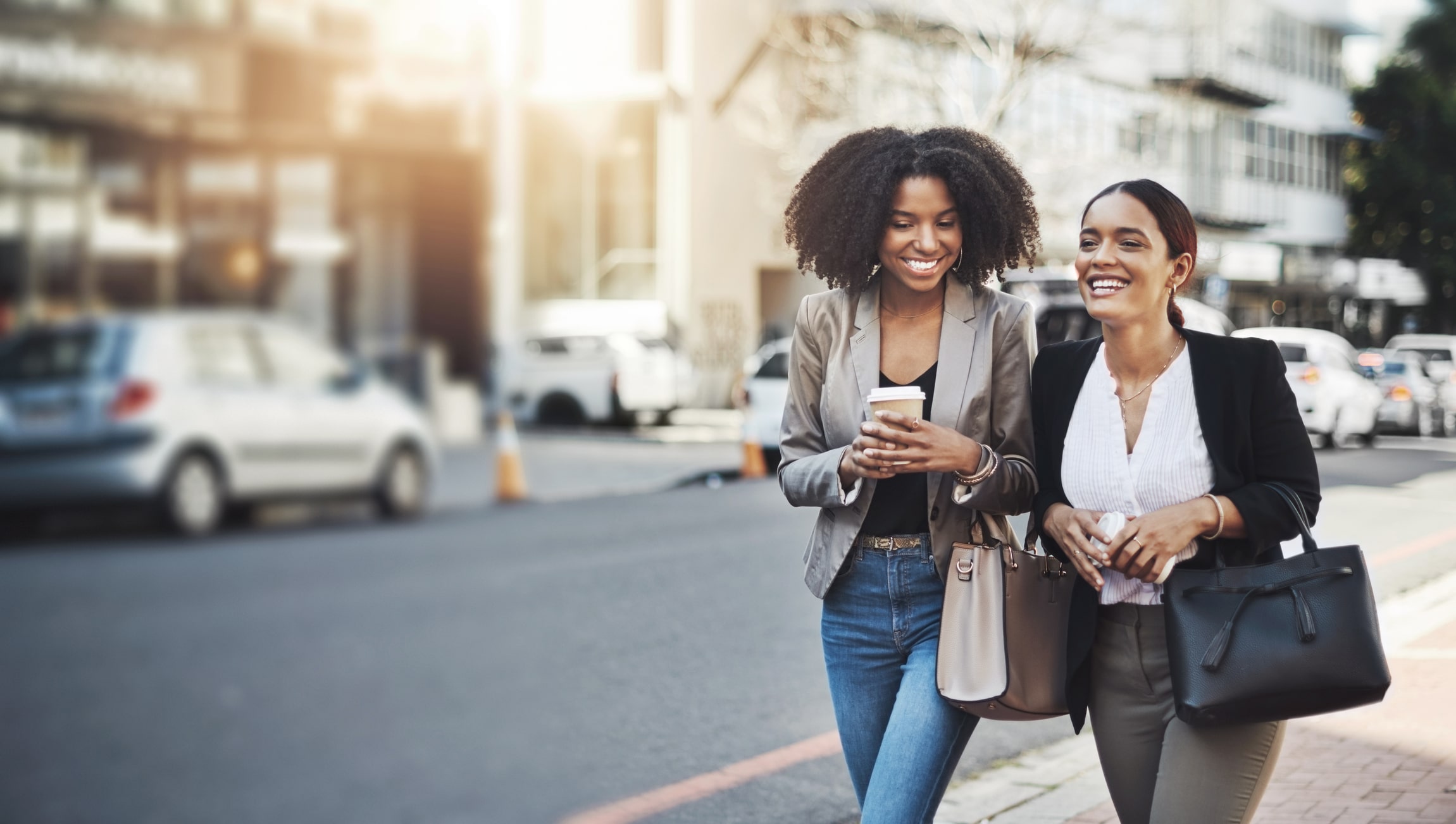 Two female friends smiling and walking down the street side by side. 