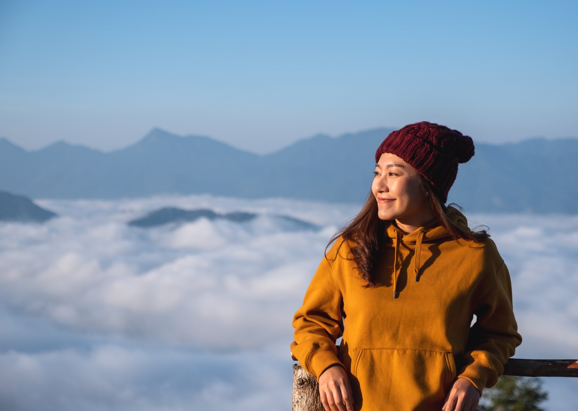 female traveling nurse stands smiling in orange hoodie in front of foggy mountain top backdrop