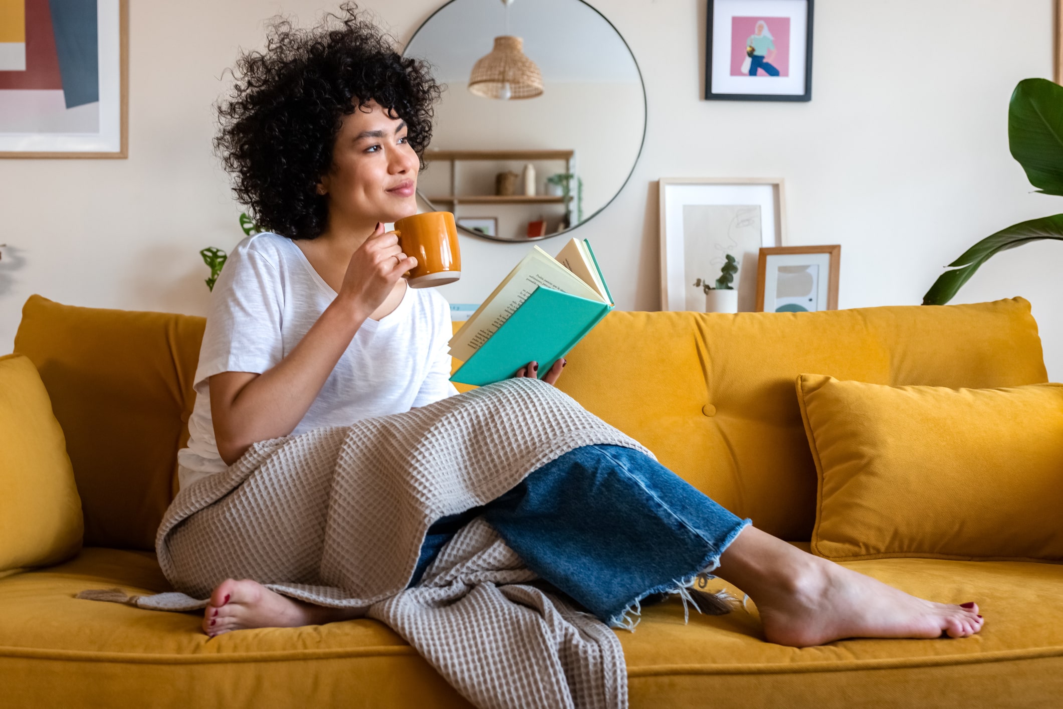 Woman relaxing on the couch while reading a book and drinking coffee.