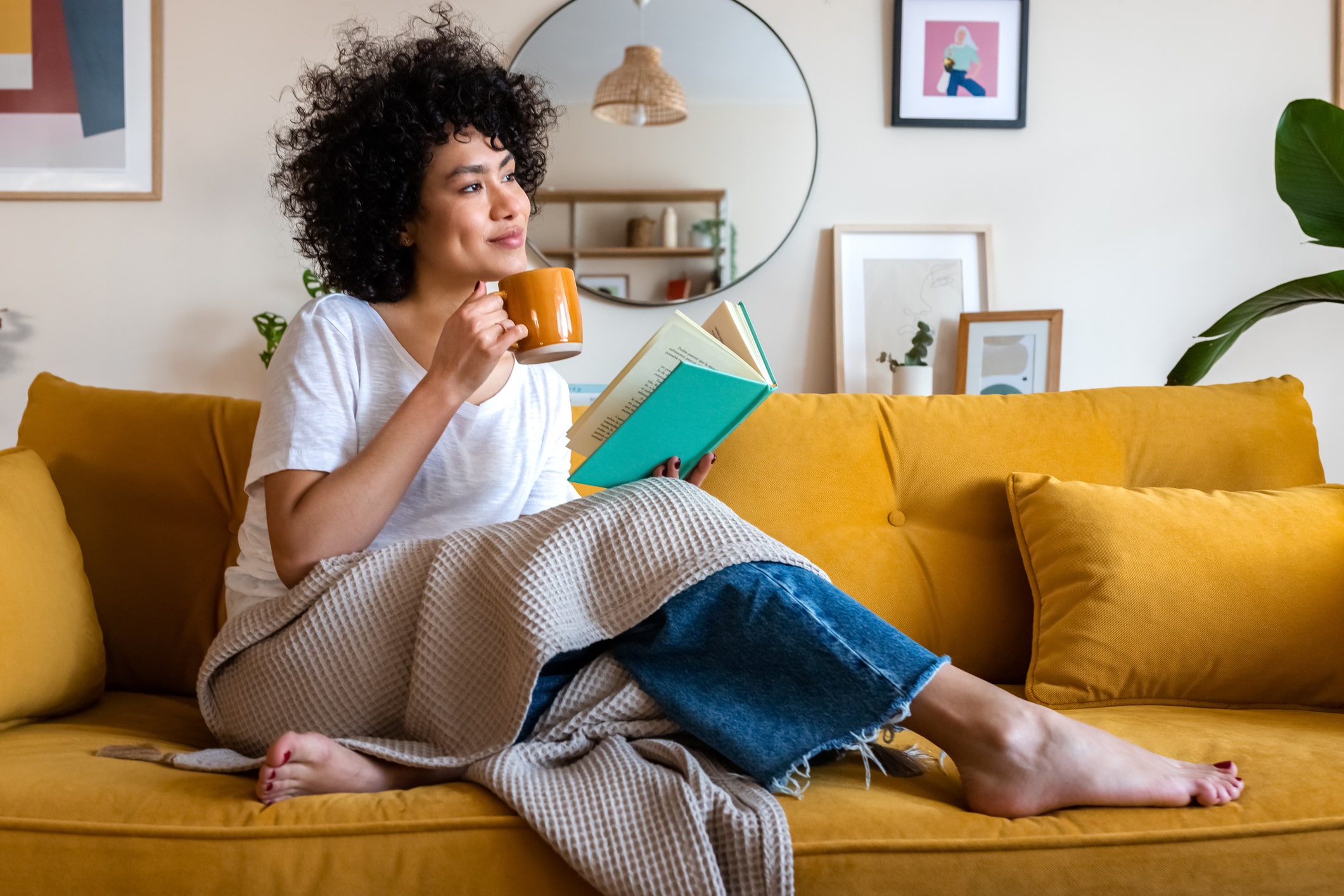 Woman relaxing on the couch while reading a book and drinking coffee. Woman relaxing on the couch while reading a book and drinking coffee.