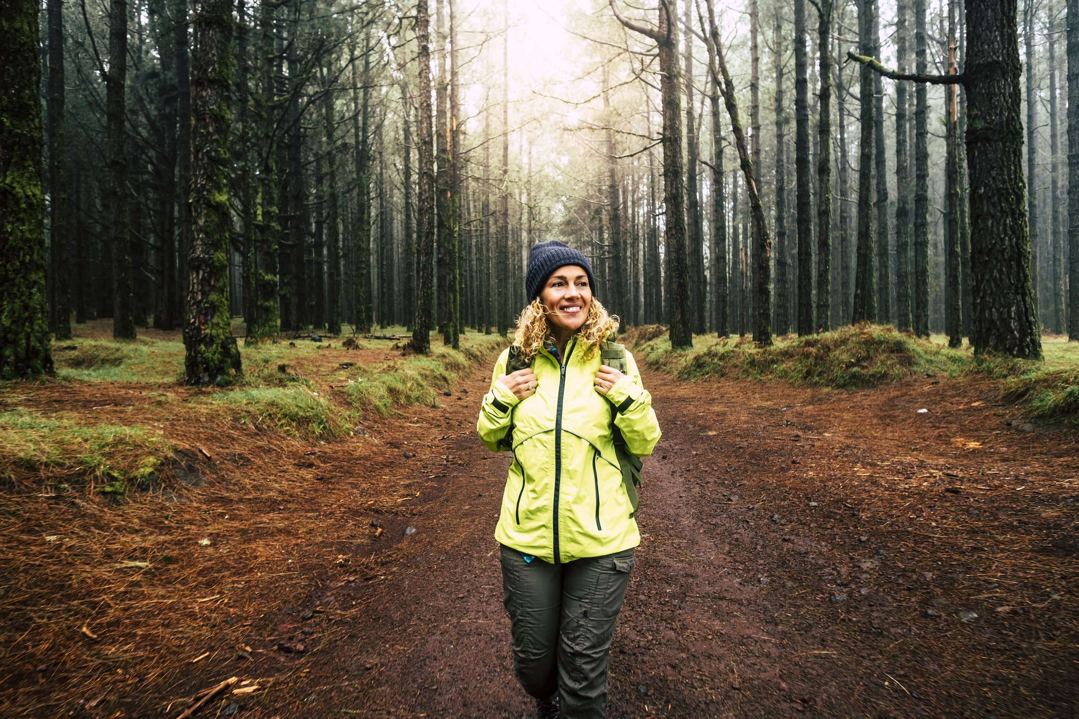 Happy female hiker smiling and enjoying nature while walking in a forest with high trees.